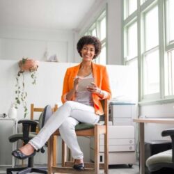 Aws Woman With Orange Blazer On Sitting In An Office Setting Smiling