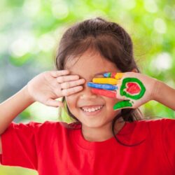 Aws Little Girl Smiling While Covering Her Eyes With Paint On Her Palms
