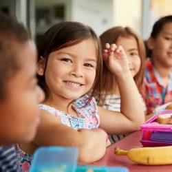 Aws Little Girl Smiling While Sitting At Lunch Table