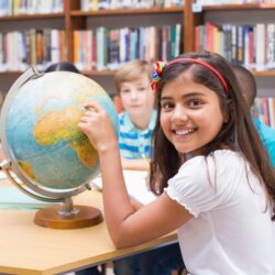 Smiling Student Pointing At A Globe In A Library