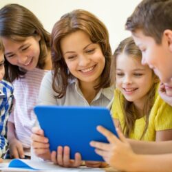 Teacher With Smiling Students Gathered Around Tablet