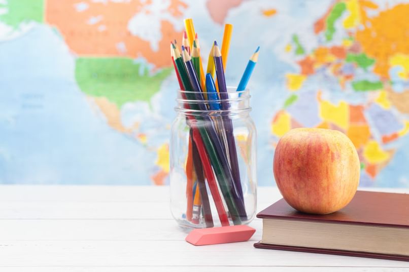 Colored Pencils In Mason Jar Next To Books C Eraser C And An Apple On Top Of A Book