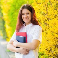 Girl Wearing White Blouse Smiling With Textbooks Infront Of Yellow Flowers