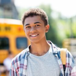Teenage African American Student In Front Of School Bus
