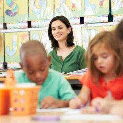 Female Teacher Smiling At Working Students