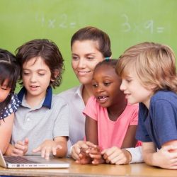 Teacher With 4 Students Gathered Around A Laptop Smiling