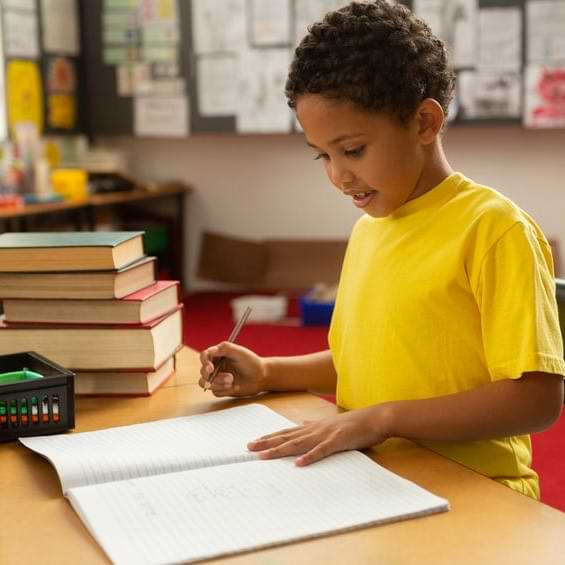 Boy In Yellow Shirt Writing In A Journal With Textbooks Next To Him