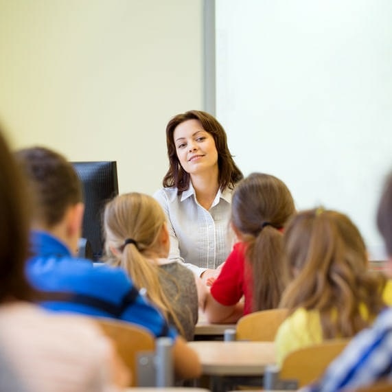 Female Teacher Smiling While Looking Over Students From The Front Of Class