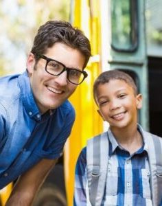 Young Male Student Smiling At The Door Of A School Bus