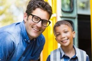 Young Male Student Smiling At The Door Of A School Bus